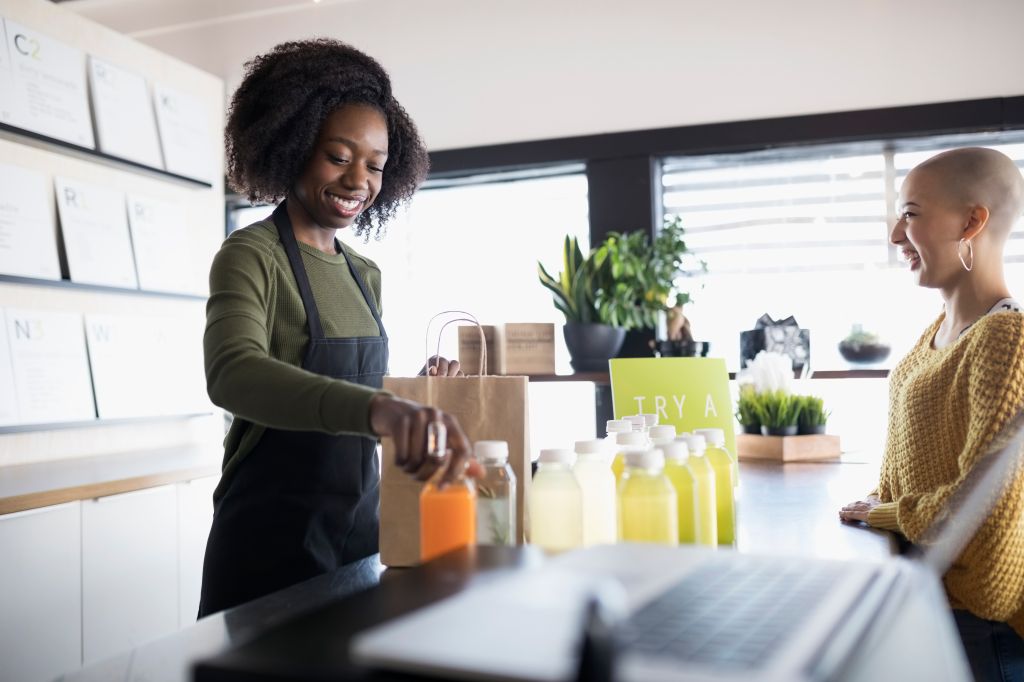 Young woman working, helping customer at juice bar