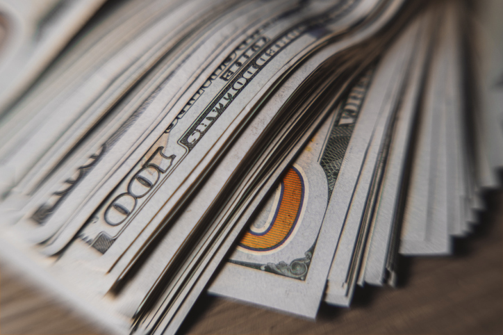 A pile of paper money: American dollars in denominations of $100 and $100 bills. A stack of crumpled bills on a wooden oak table, close-up, blurred, with selective focus.